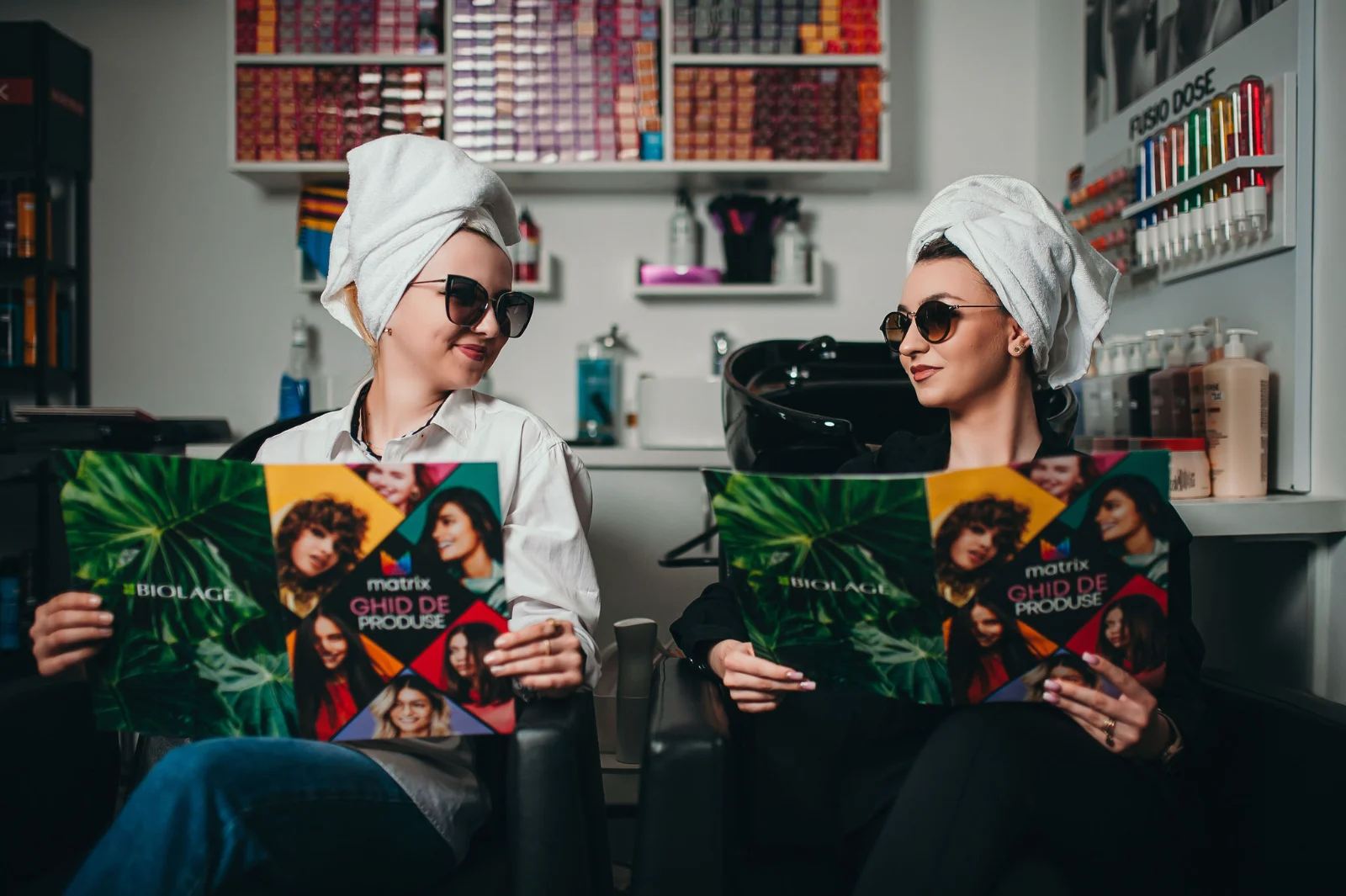 Două cliente se relaxează în salon, răsfoind reviste